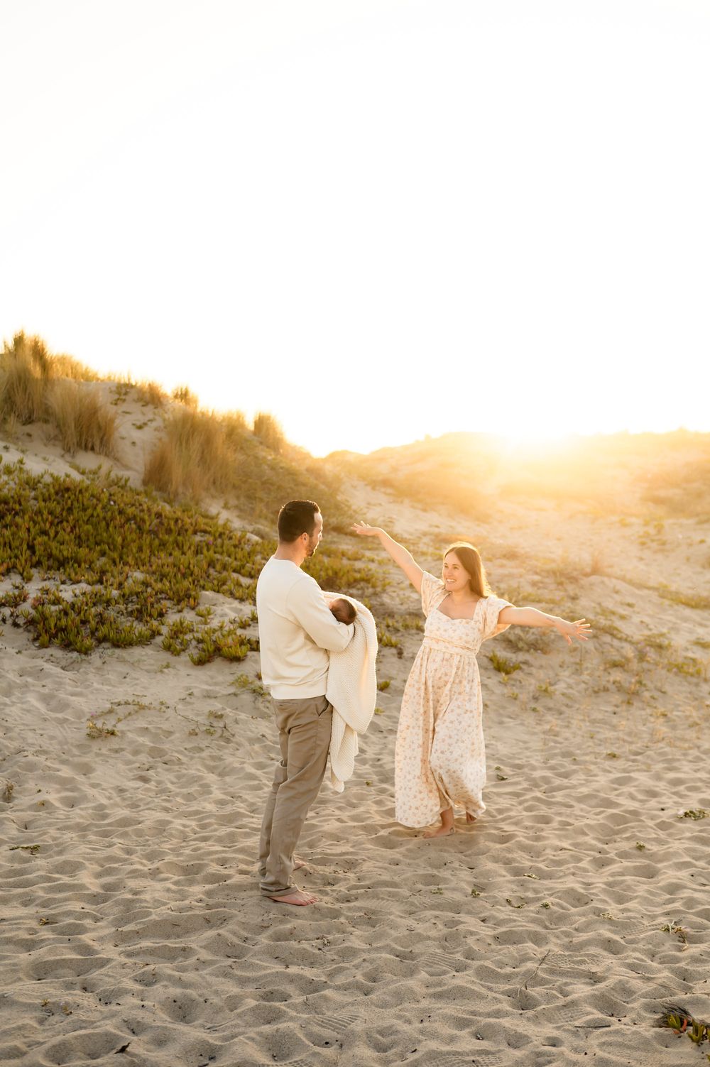 Couple holds and dances with their newborn baby during golden sunset beach newborn photoshoot in Ventura, captured by Ventura photograper