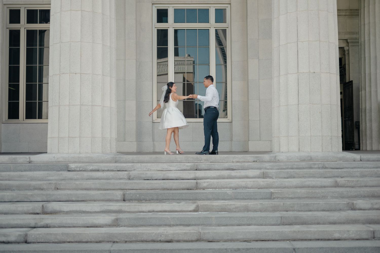 Bride and groom exit a grand courthouse with white columns and stone steps after their wedding ceremony.