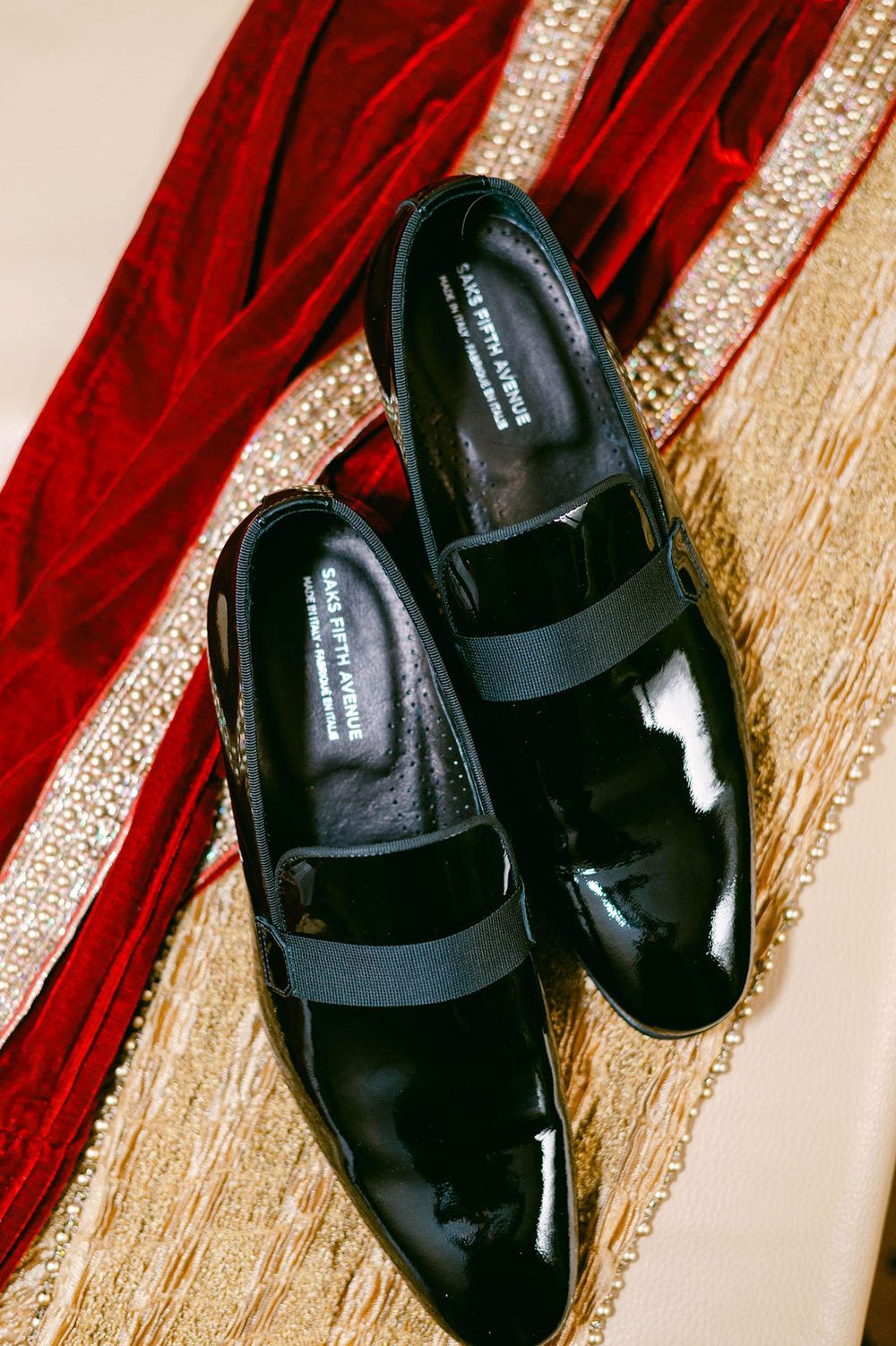 Black patent leather dress shoes on red and gold textured fabric.