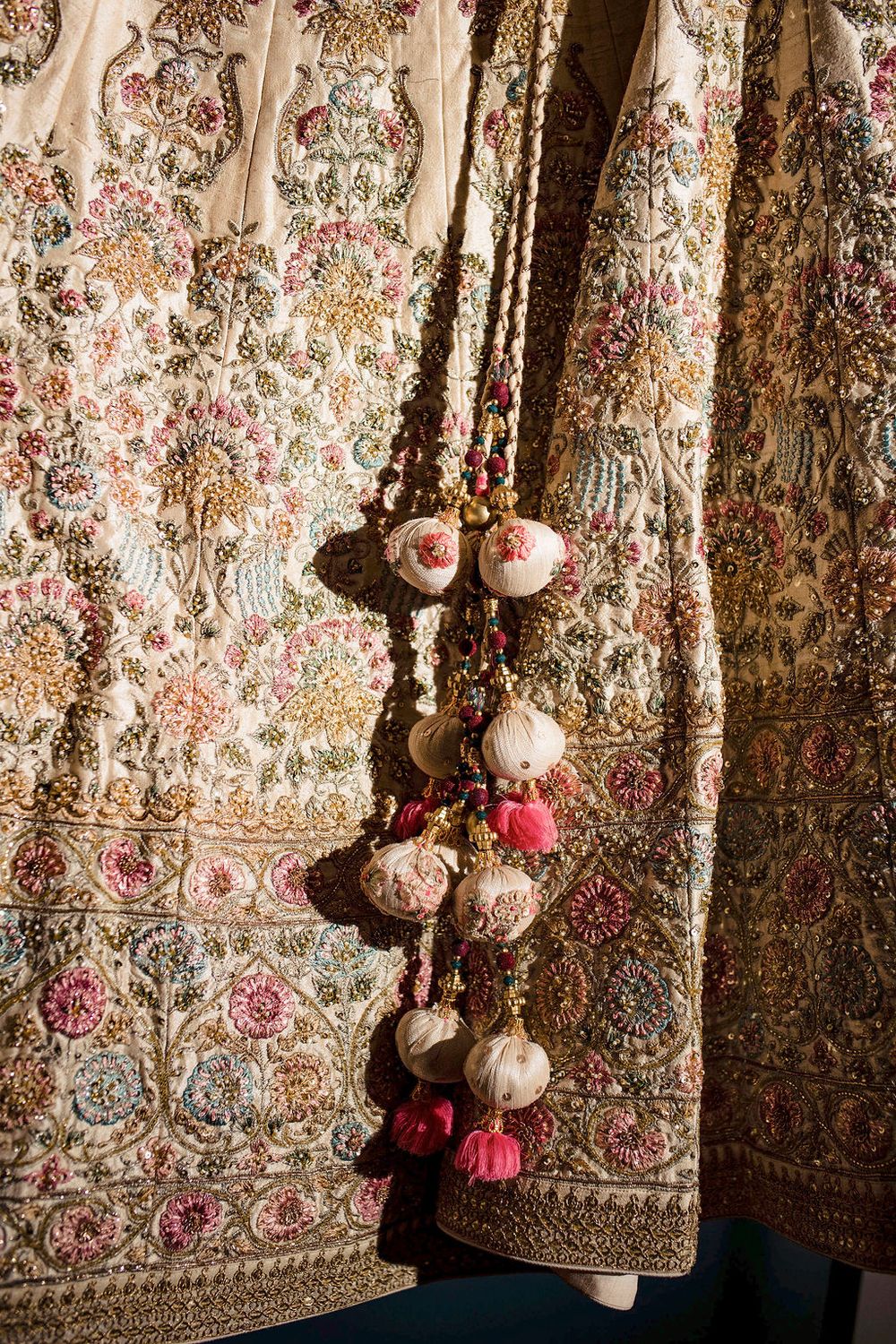Ornate floral embroidered fabric with decorative tassels and beaded embellishments in pink and gold tones.