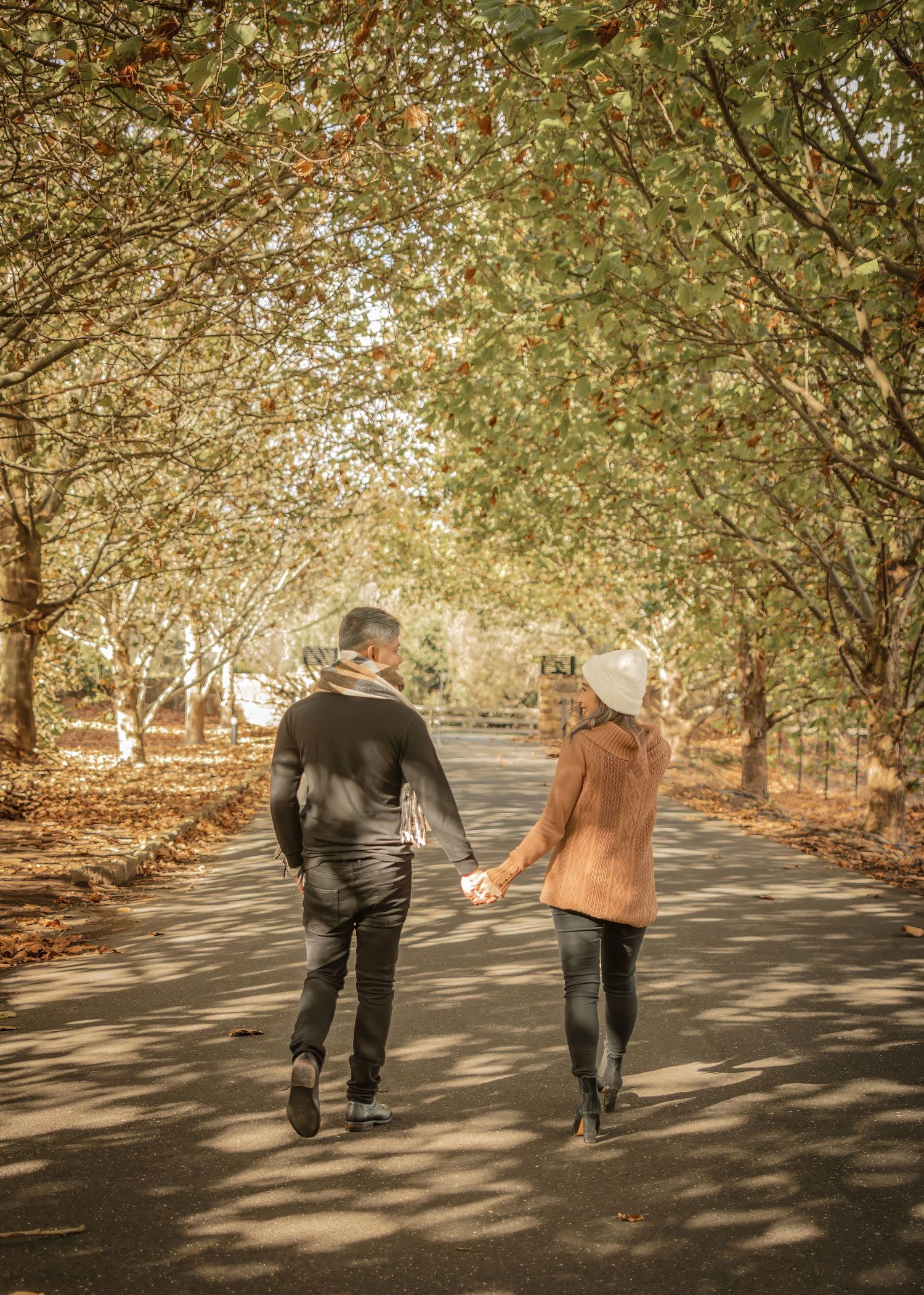 Couple walking away on tree-lined path with dappled sunlight creating romantic autumn atmosphere.