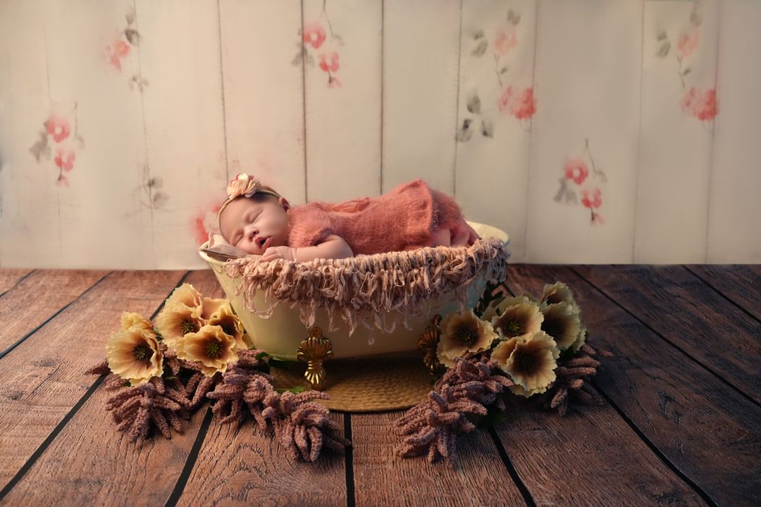 A newborn baby sleeps peacefully on a pink textured blanket in a soft natural light setting.