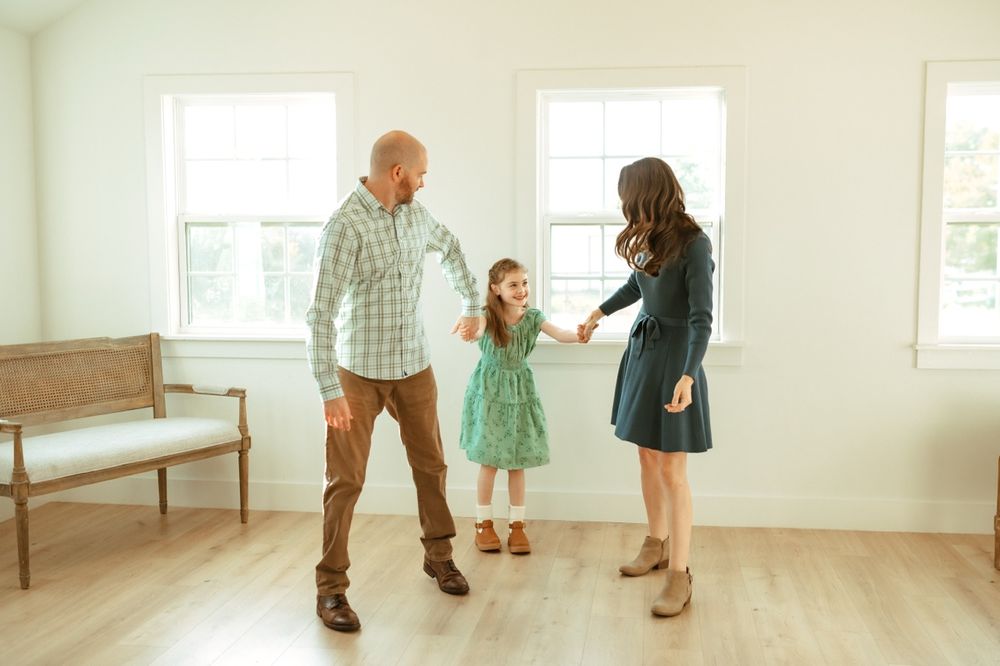 Family playing and dancing together in a bright minimalist room with hardwood floors.
