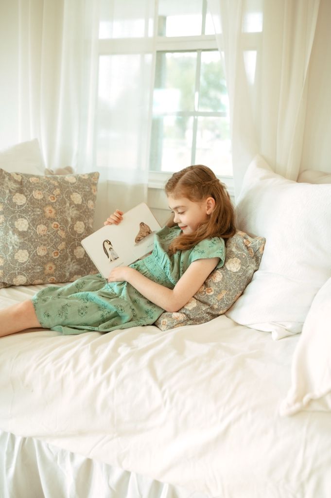 A series of photos showing someone in a mint green dress reading while lying on a white bed with floral pillows.