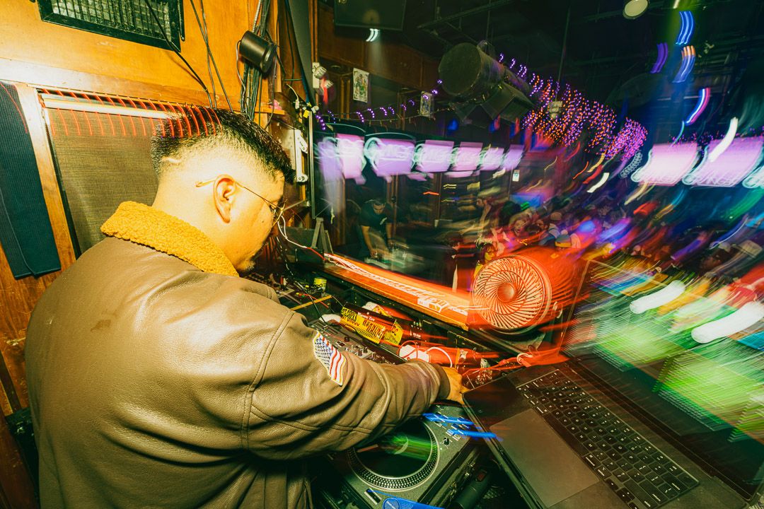 DJ performs at a vibrant nightclub with colorful lighting and electronic equipment setup.