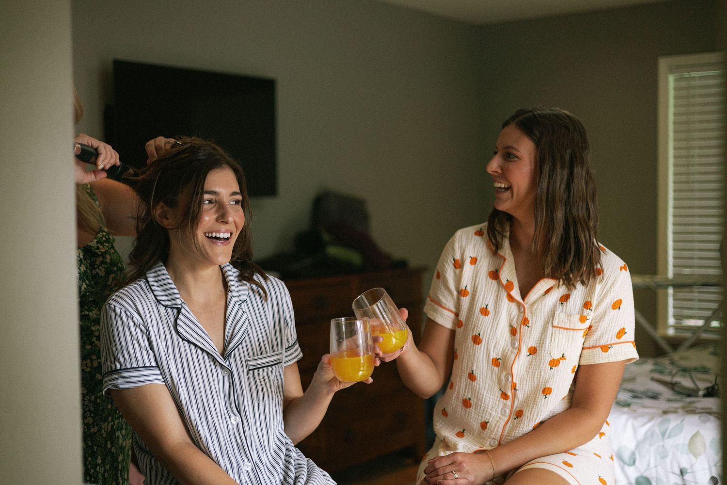 Two friends in pajamas laughing and enjoying drinks together during a casual hangout at home.