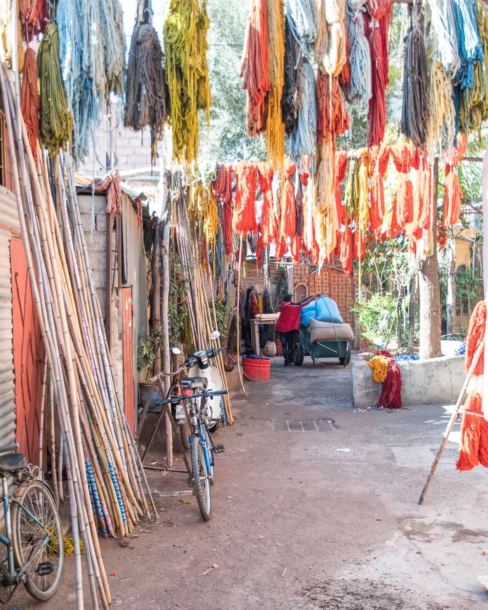 Brightly coloured dyed yarn hanging above a Marrakech street beside workshop entrances.