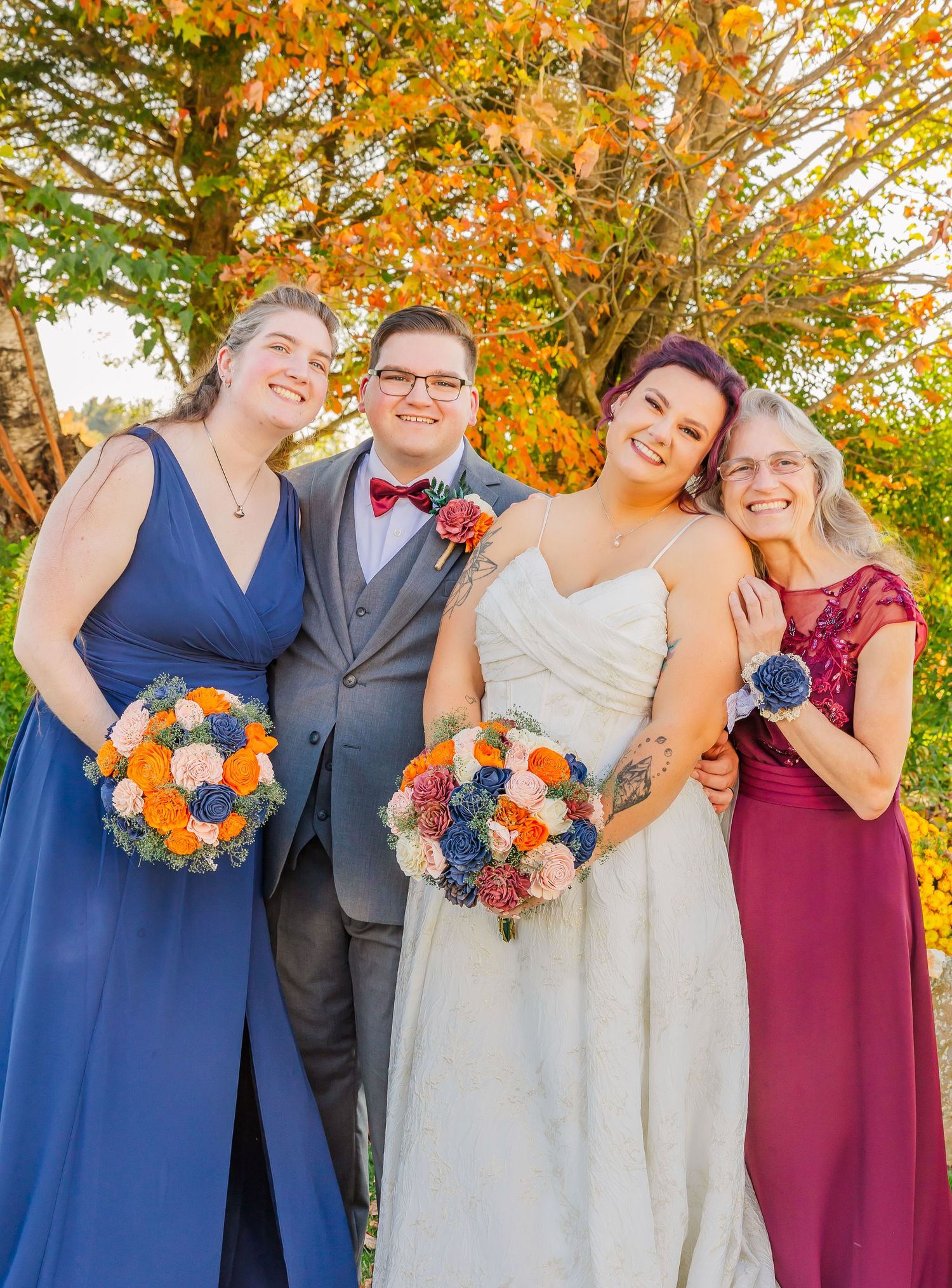Wedding party poses together outdoors with colorful fall foliage and bright orange and blue bouquets.