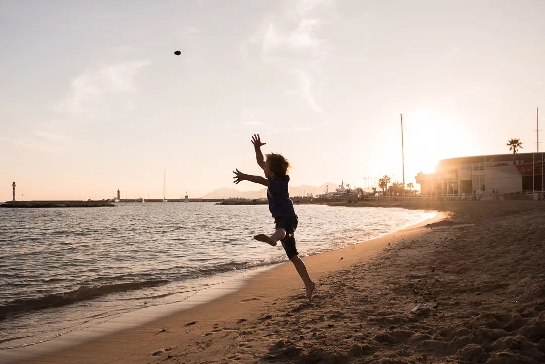 A boy jumping on the beach at sunset, captured in silhouette.