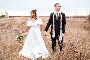 Couple walking through tall grass field in wedding attire.