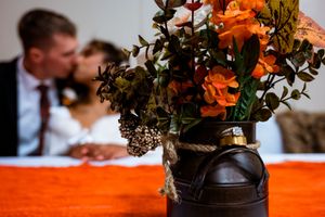 Orange floral centerpiece in a dark vase on a table with blurred background at a wedding reception.