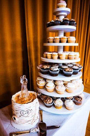 A rustic wedding dessert display featuring tiers of cupcakes and a birch-themed wedding cake on white stands.