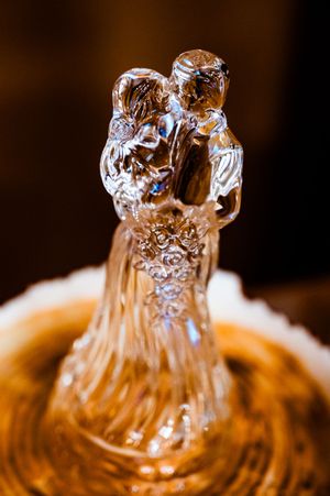 Crystal wedding cake topper figurine with intricate details glowing in warm light.