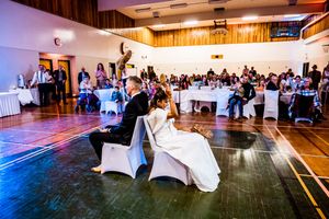 Wedding reception in a rustic wood-paneled venue with guests seated at decorated white tables.