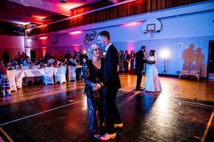 Couples dancing on a wooden floor under dramatic red and blue lighting at an indoor reception.