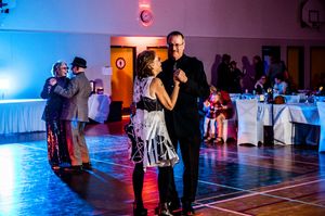 Couples dancing in a dimly lit ballroom with blue and purple lighting creating a romantic atmosphere.