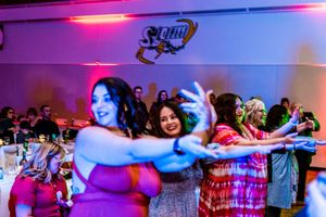 People dancing and celebrating at a lively party with colorful pink and blue lighting effects.
