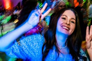 A person in a blue sparkly top dances under colorful nightclub lighting at a party.