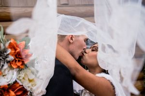 Wedding party poses with veils blowing in the wind against rustic backdrop.