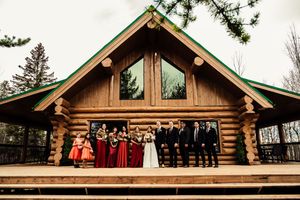 Wedding party posed on the deck of a log cabin venue.