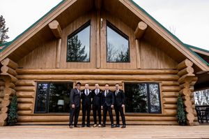 Wedding party sitting on the steps of a rustic log cabin venue.