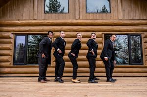 Groomsmen relaxing on wooden steps of a log cabin building.