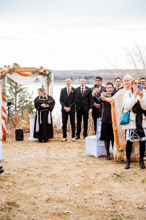 Wedding party poses playfully in a line outdoors during autumn with orange decorations and natural scenery.