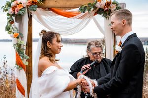 Outdoor wedding ceremony under wooden arch decorated with orange flowers and white fabric.