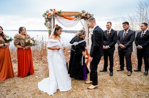 Outdoor wedding ceremony under floral arch with orange and peach blooms.
