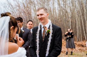 Winter wedding ceremony with orange and white decor against a backdrop of bare trees.