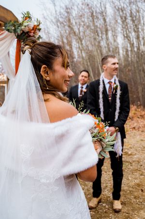 A winter wedding ceremony with fur shawls and orange floral accents set against bare trees in the background.