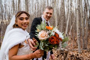Autumn wedding ceremony with orange floral decorations and white chairs set up in wooded outdoor setting.