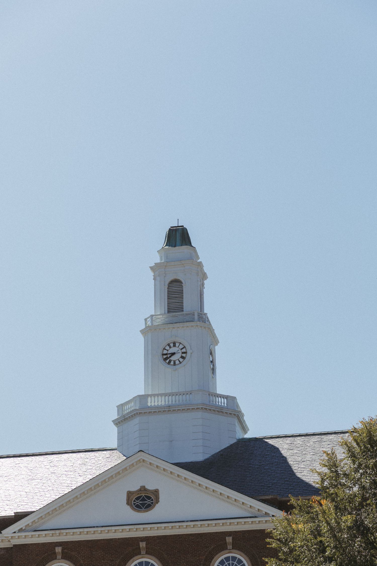 White clock tower with colonial architectural features sits atop a building against a blue sky.