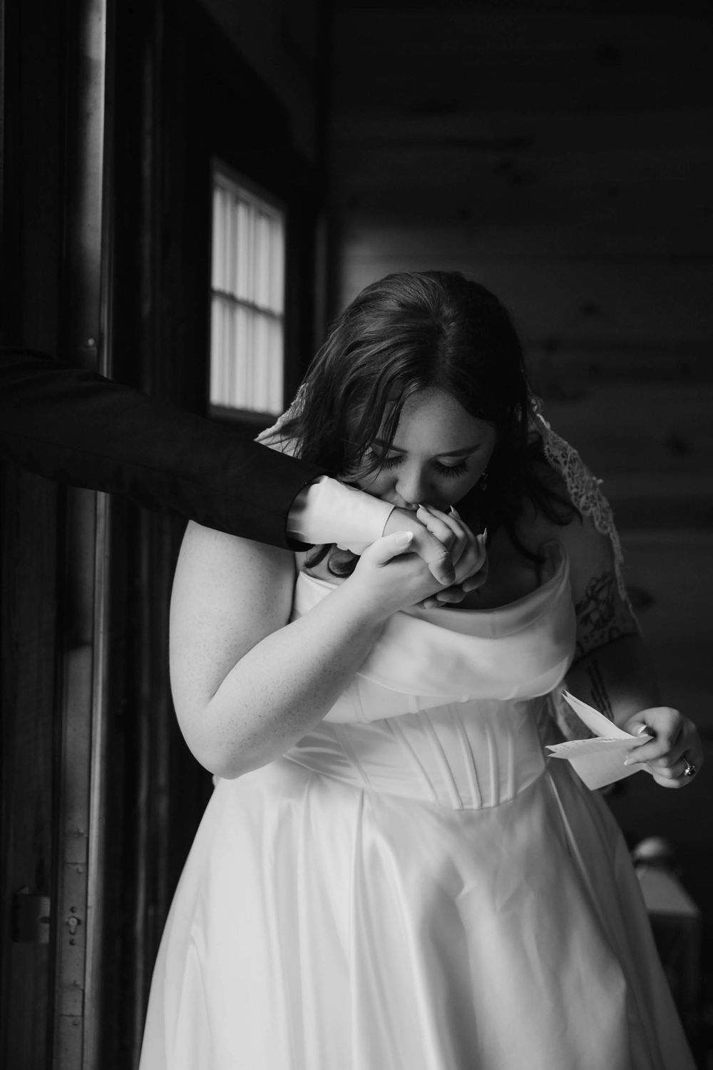 Emotional black and white photo of bride crying while reading letter during wedding day first look.
