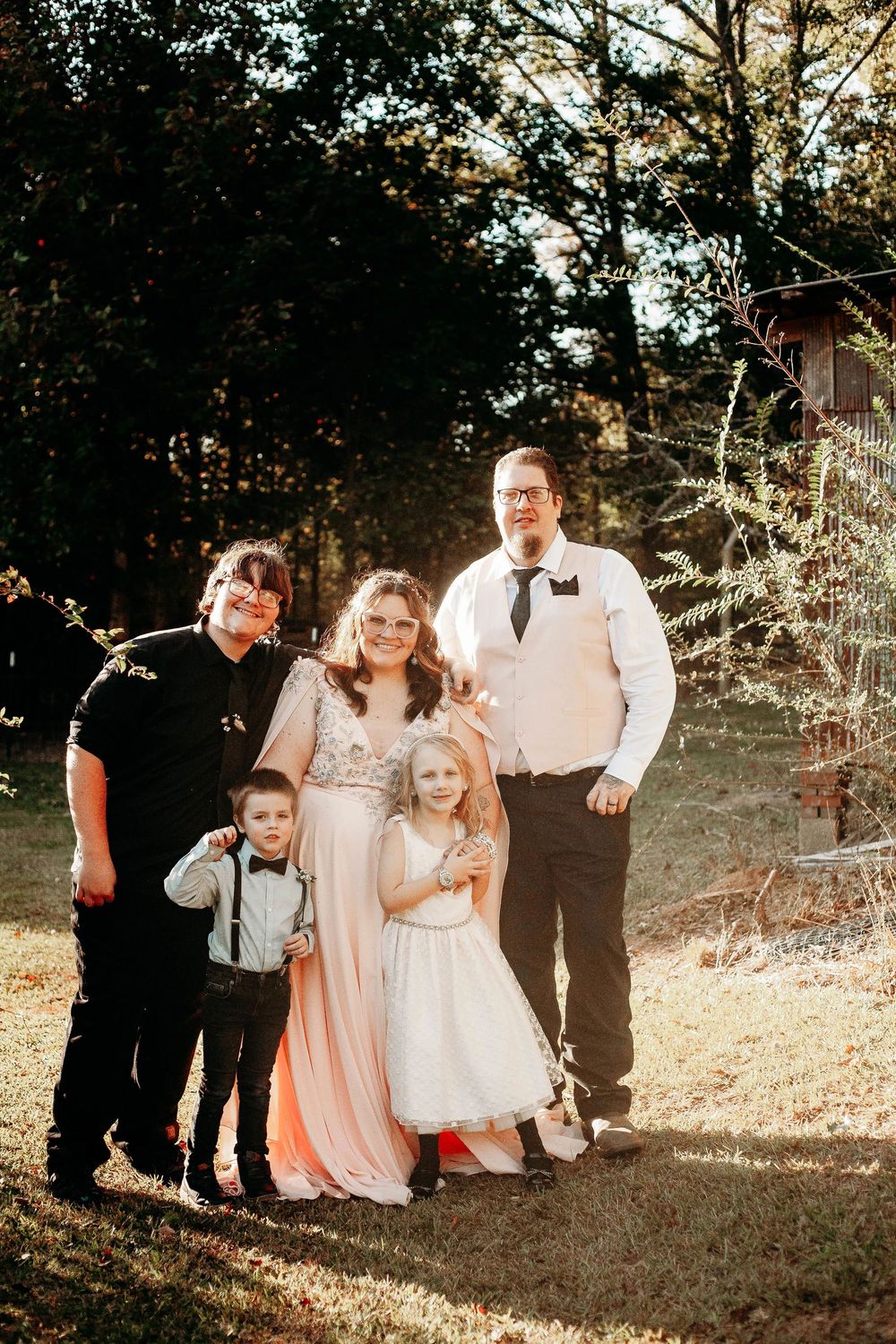 Family portrait with bride, groom, and three children in autumn woodland setting.