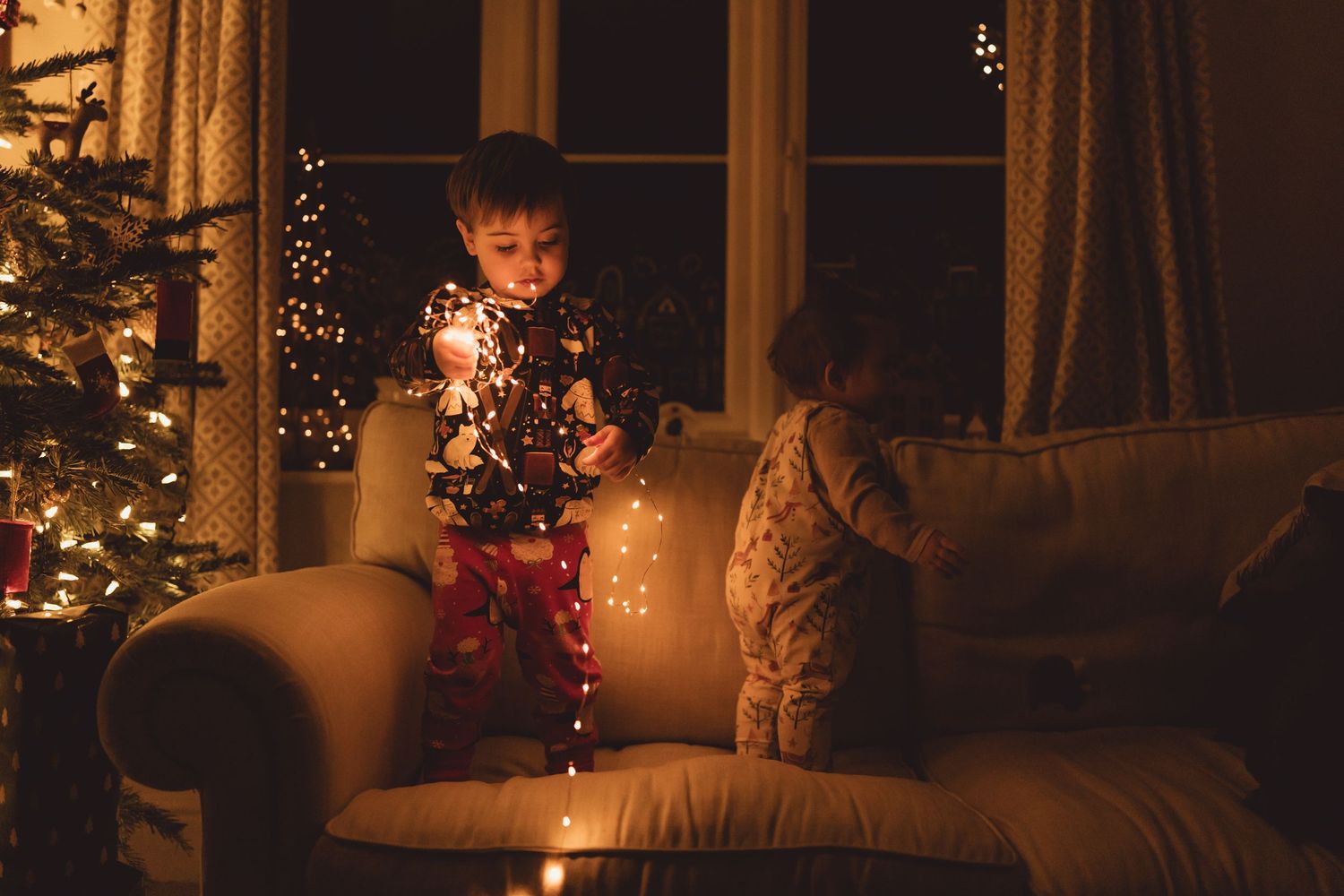 A cozy Christmas living room decorated with twinkling lights and a glowing tree in the evening.