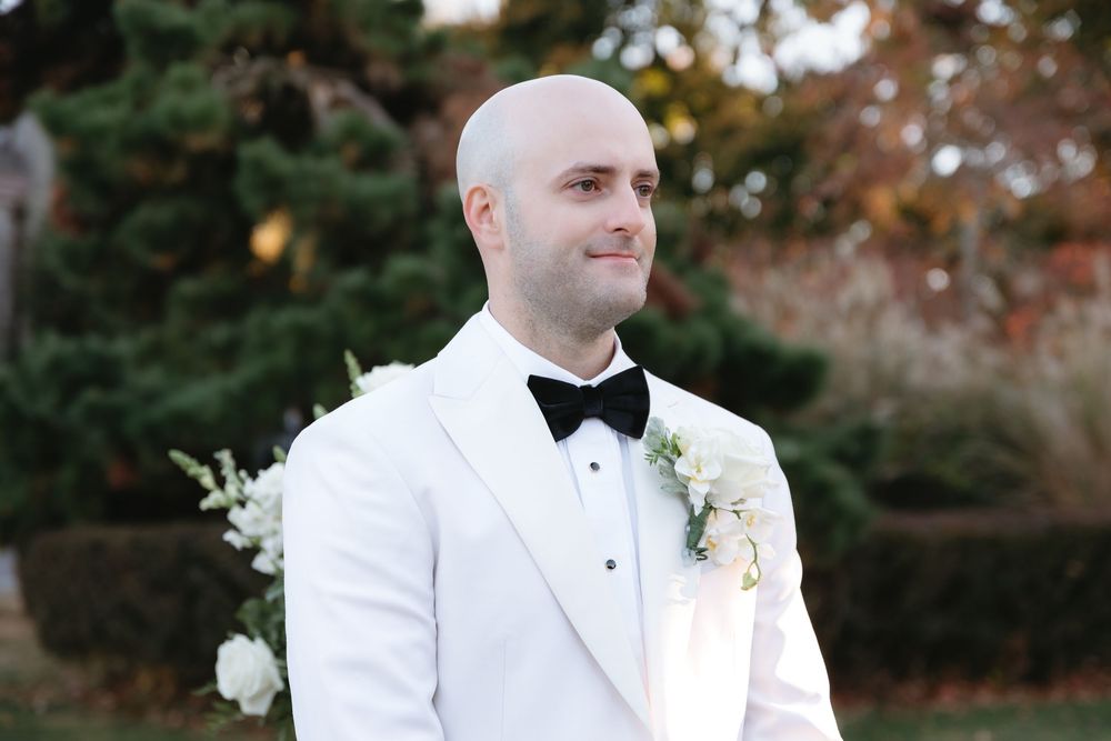 Wedding couple in white formal attire pose elegantly outdoors during their special day.