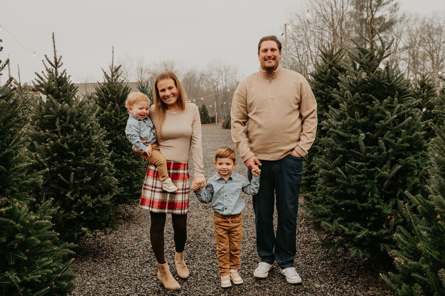 Family walking together through a Christmas tree farm in New Jersey, smiling and holding hands during a festive holiday photo session