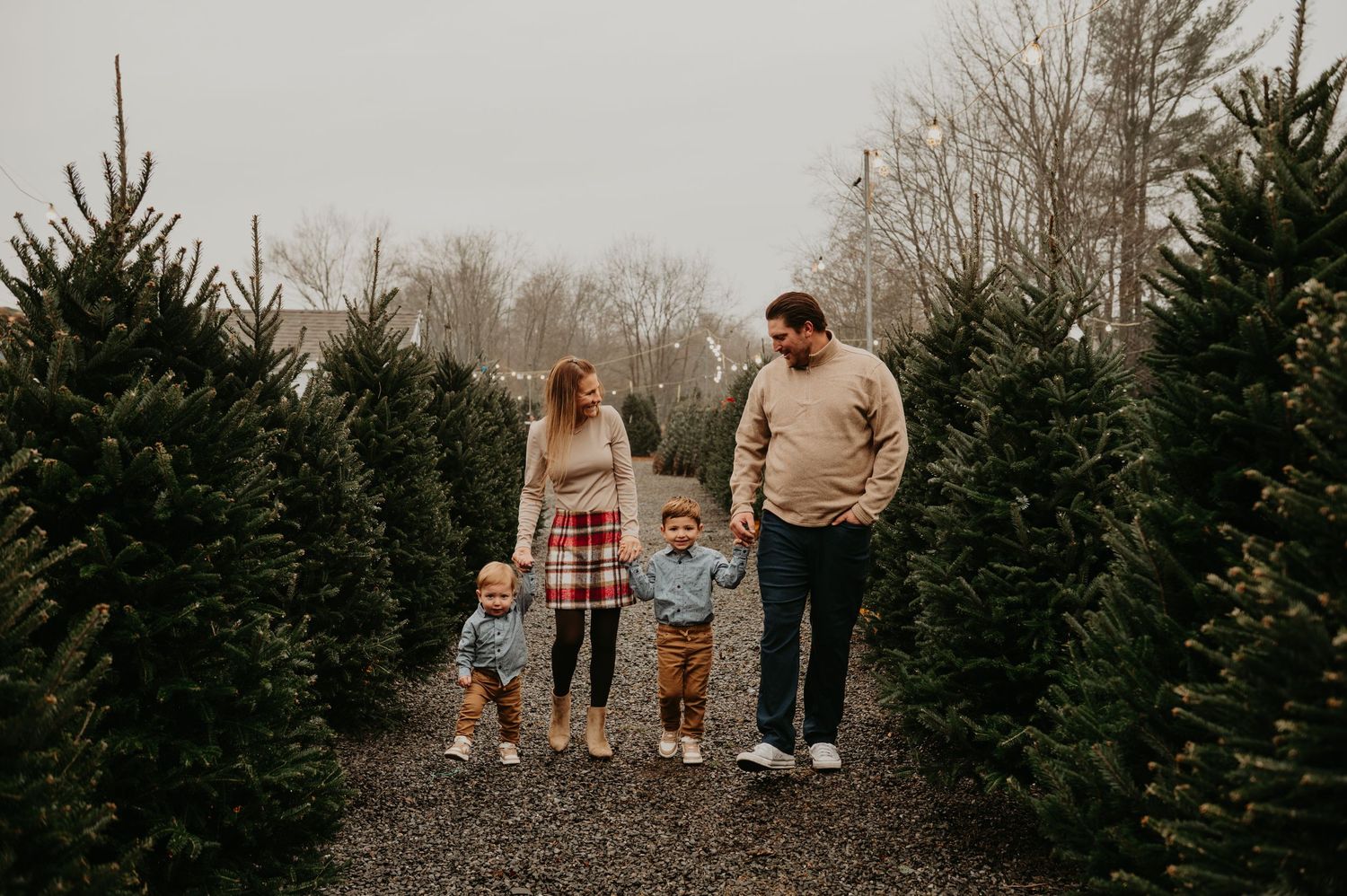 Family walking together through a Christmas tree farm in New Jersey, smiling and holding hands during a festive holiday photo session