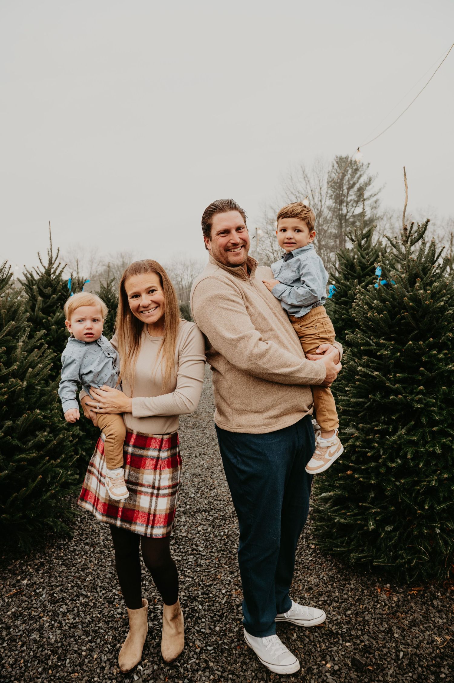 Family walking together through a Christmas tree farm in New Jersey, smiling and holding hands during a festive holiday photo session