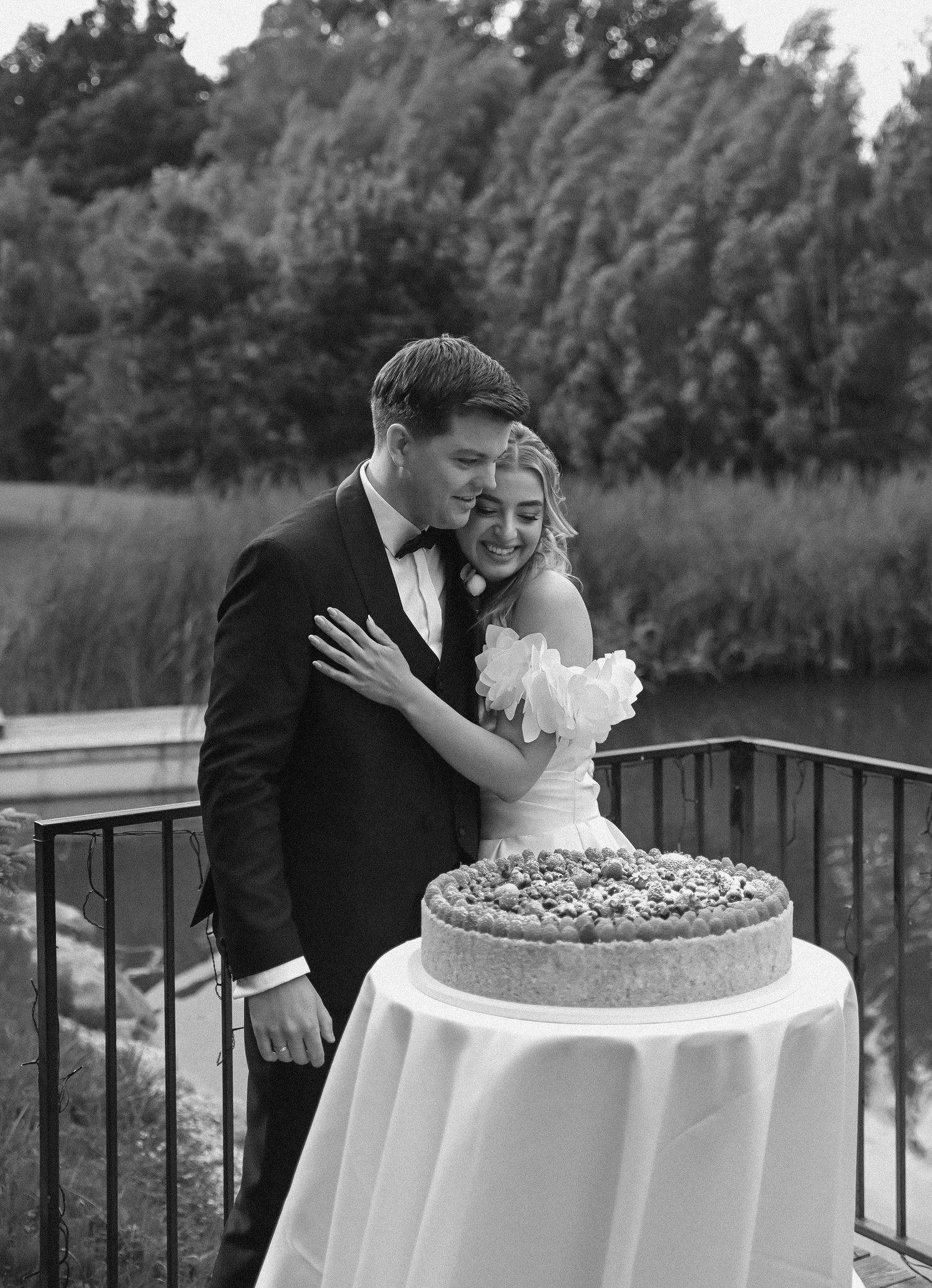 Romantic black and white wedding photo sequence showing couple sharing intimate moments beside elegant tiered cake.