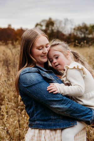 Two people in denim and cream sweaters share tender embraces while sitting in a golden autumn field at sunset.