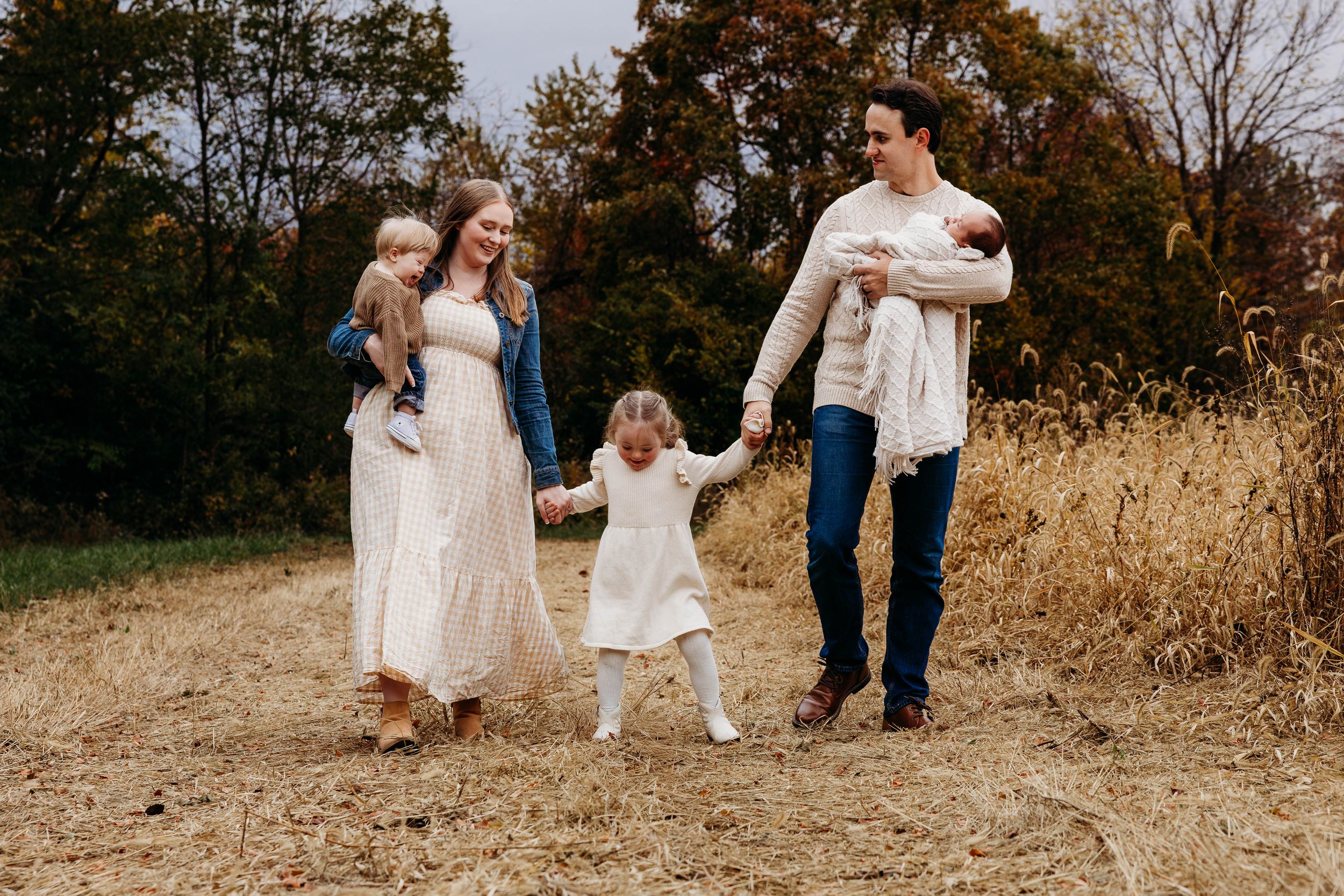 A family in white outfits walks together through a golden autumn field at sunset.