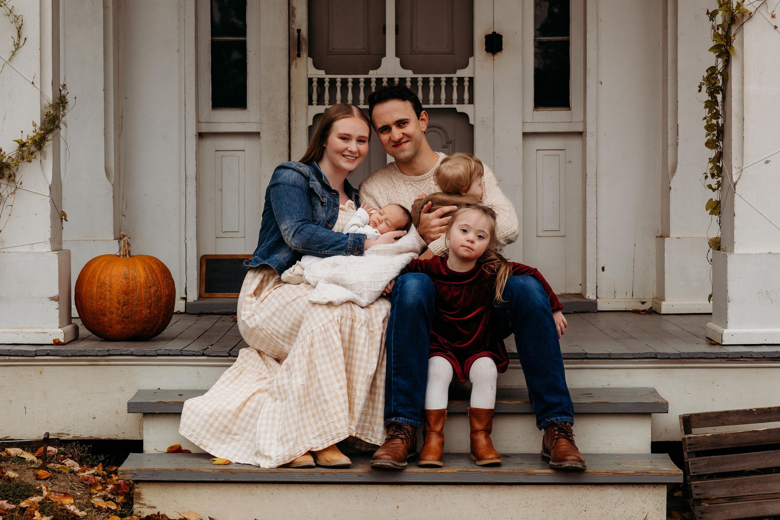 A cozy autumn scene on front porch steps with a pumpkin decoration and family sitting together.
