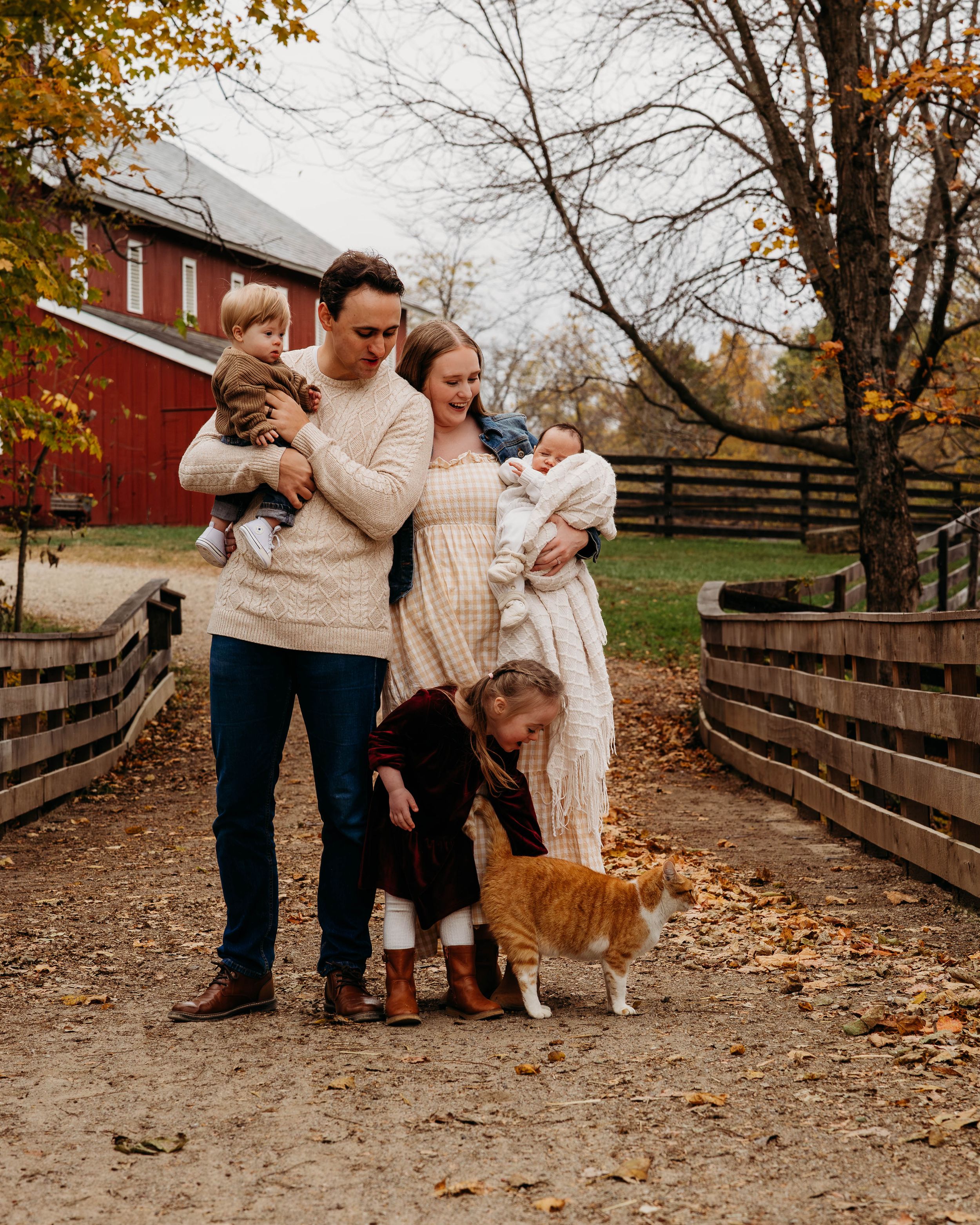 Family enjoying autumn day together on a rustic farm path lined with wooden fences and fall foliage.