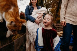 A joyful child in a velvet dress laughs outdoors while a dog peeks into frame during an autumn family photo session.