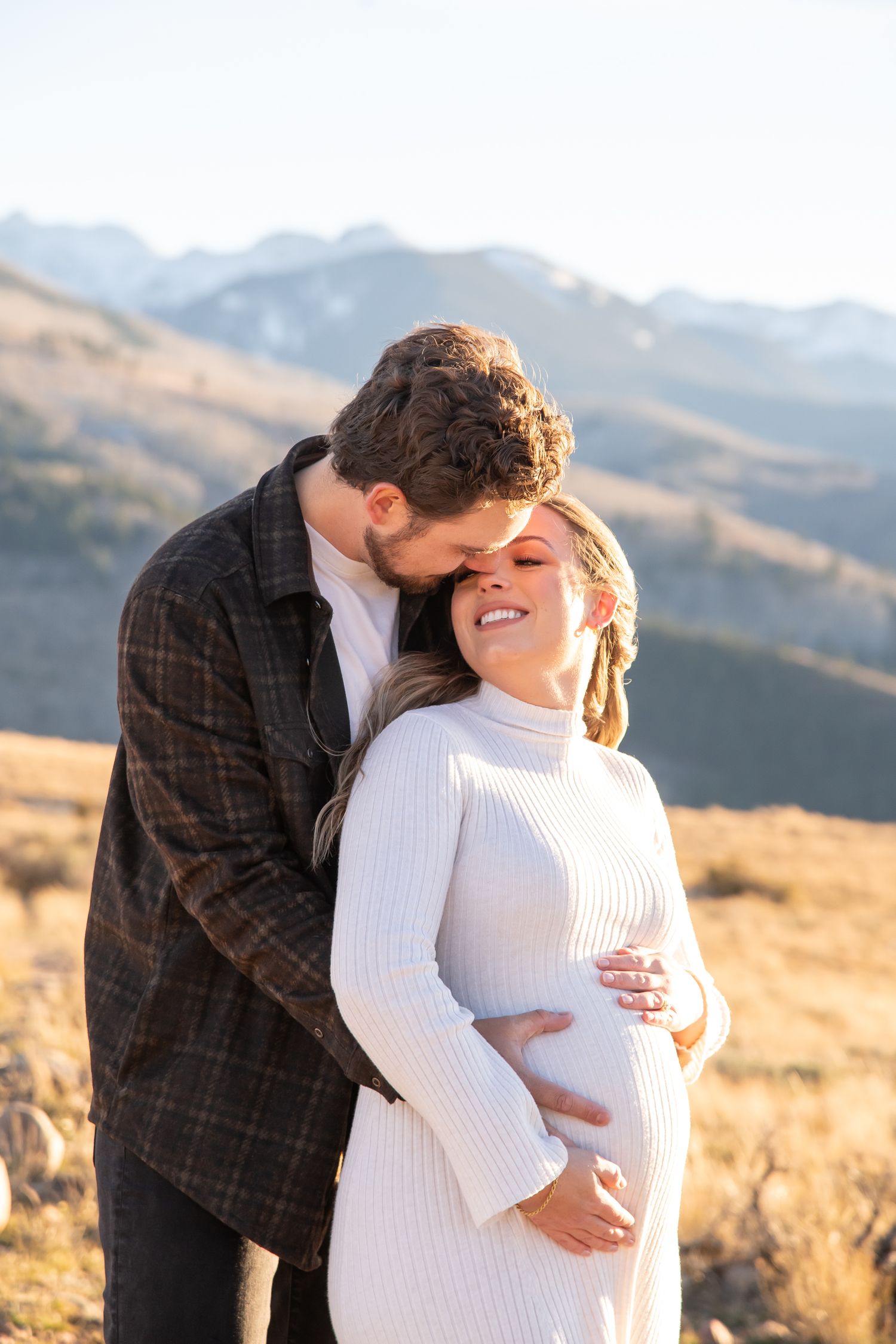 A cute couple embraces in a romantic moment against a backdrop of golden hills and mountains during sunset in Vail.