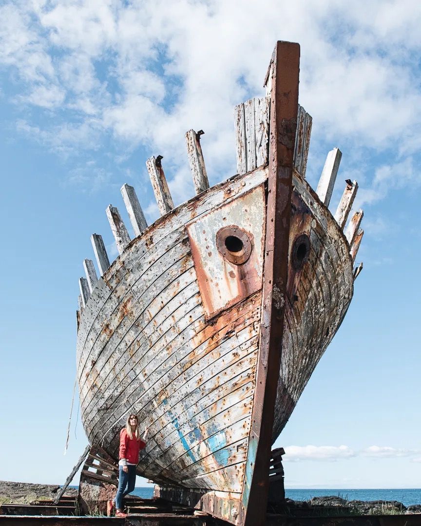 Weathered wooden boat resting on a beach under a bright blue sky.