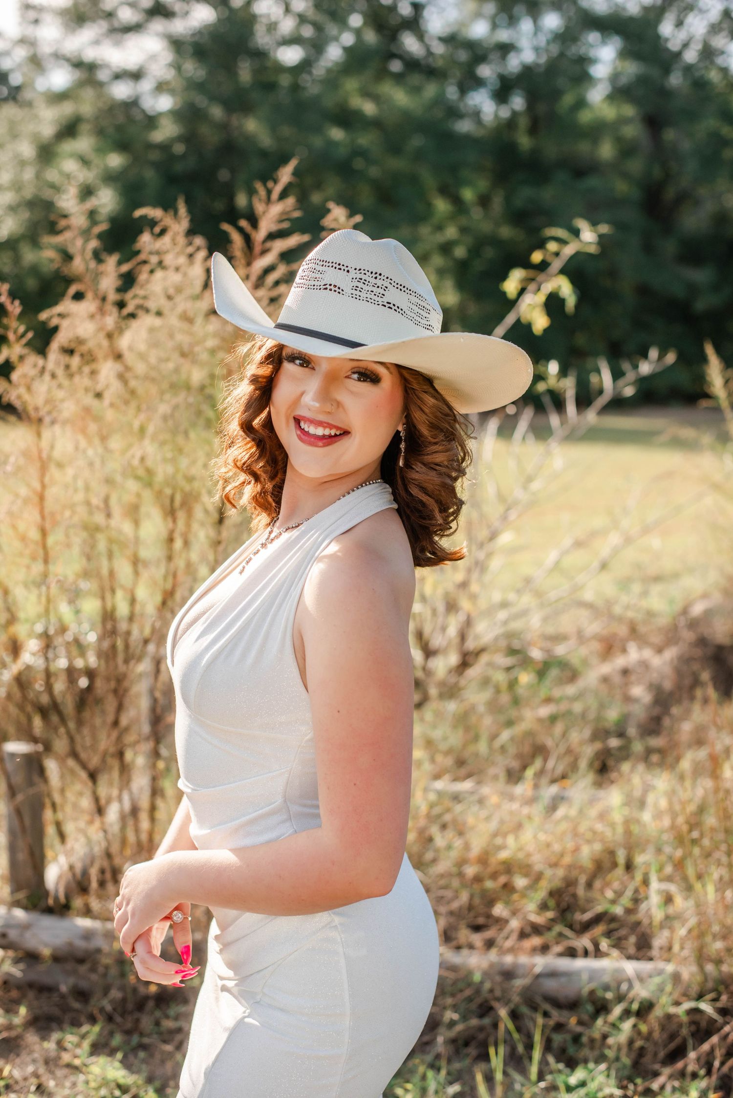 A bride in a white halter dress poses outdoors near a fountain during a wedding photoshoot at sunset.