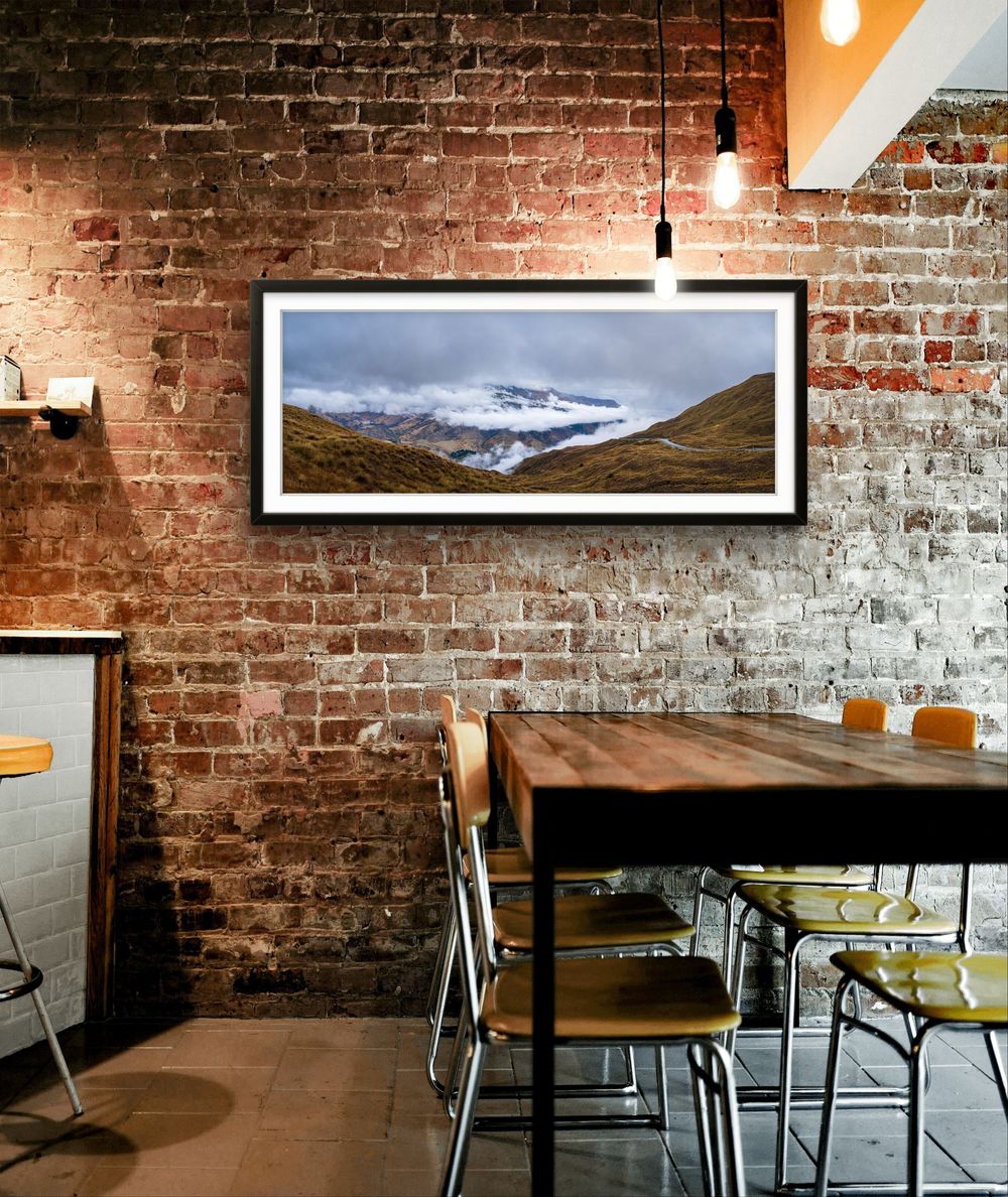 Panoramic framed landscape print of snow-capped mountains hanging on a rustic brick wall in a cafe.